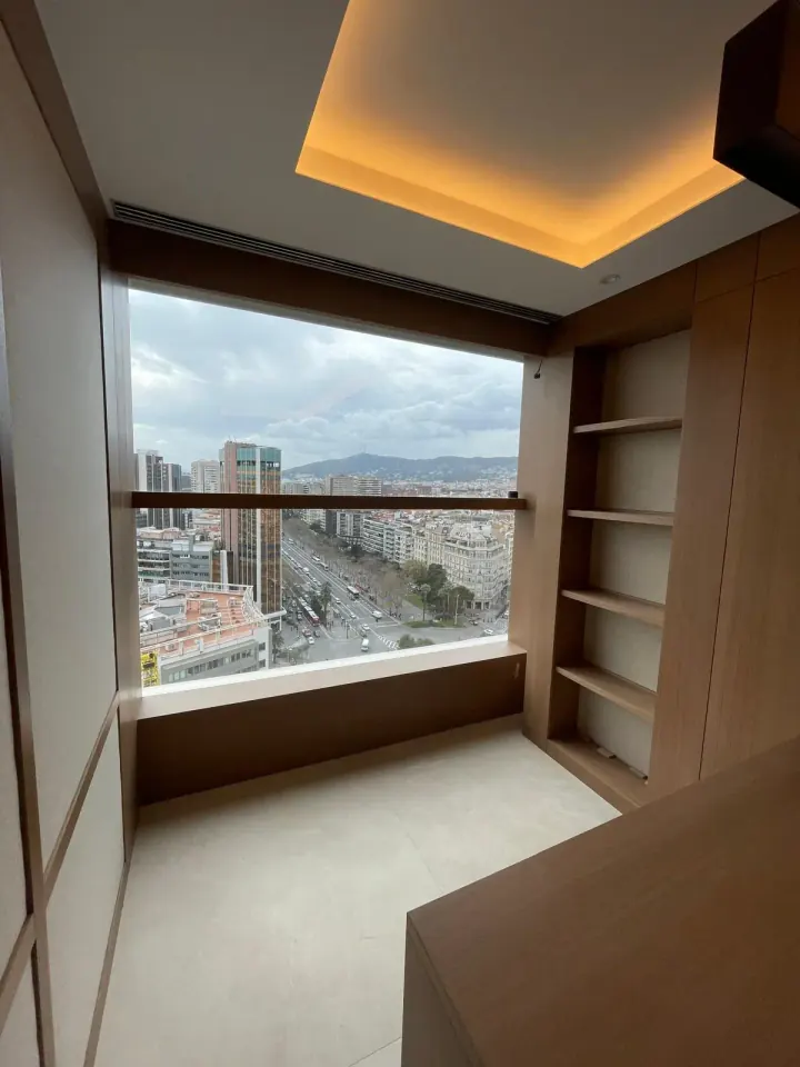 Despacho revestido de madera, con estantería junto a la ventana y vistas a Barcelona